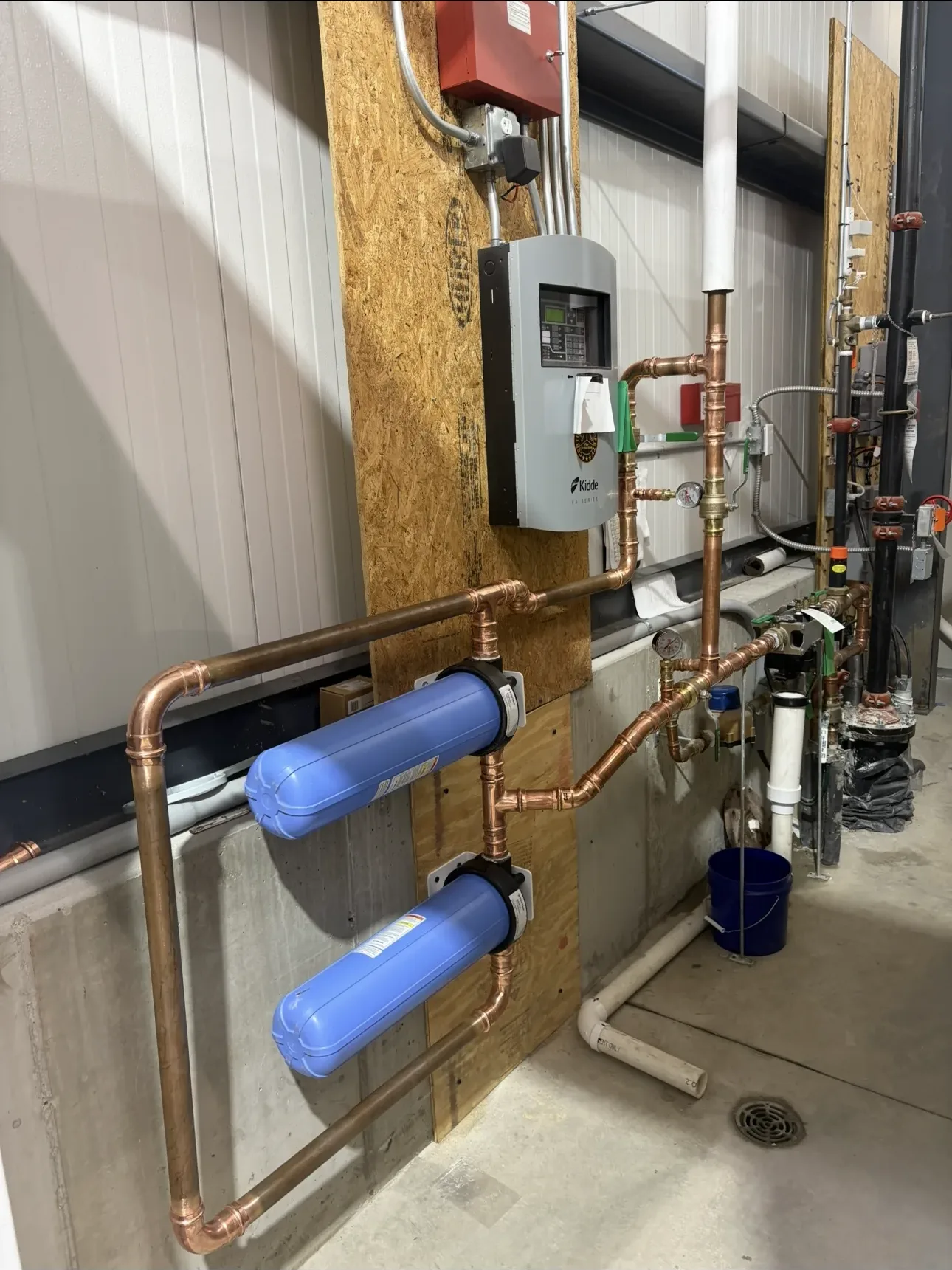 pipes, plumbing, water treatment, industrial equipment, concrete floor, wooden wall, electrical panel, copper pipes, blue tanks